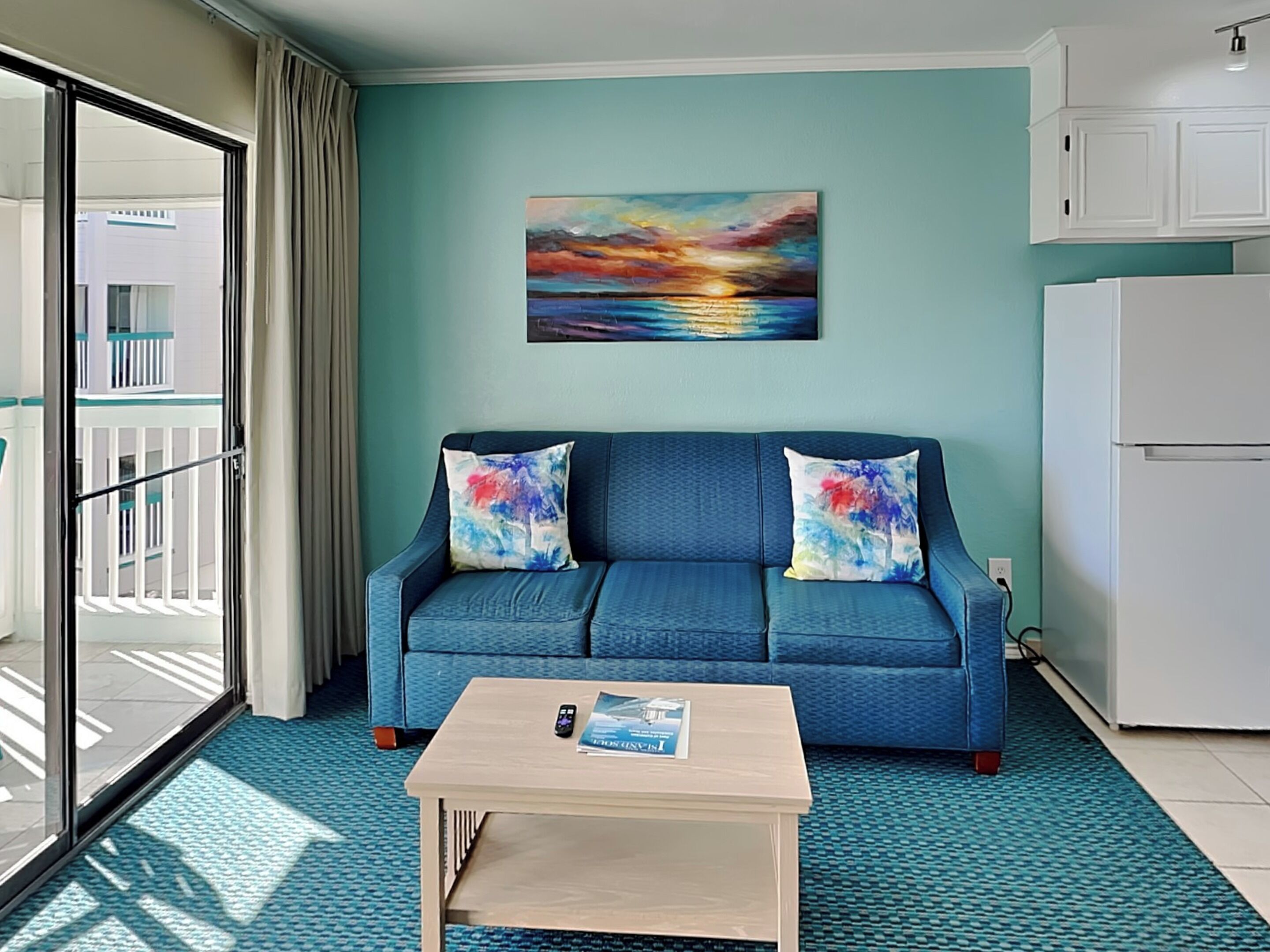 A modern living room with a blue sofa, a coffee table, and a painting of a sunset.