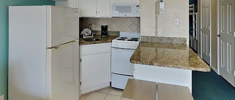 A compact kitchen with white cabinets, a white refrigerator, a stove, and a coffee maker. There is a small wooden table and a phone on the wall.