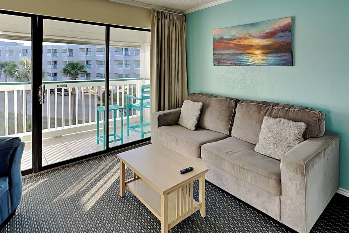 A room with a beige sofa, a small wooden table, and a painting of a sunset.