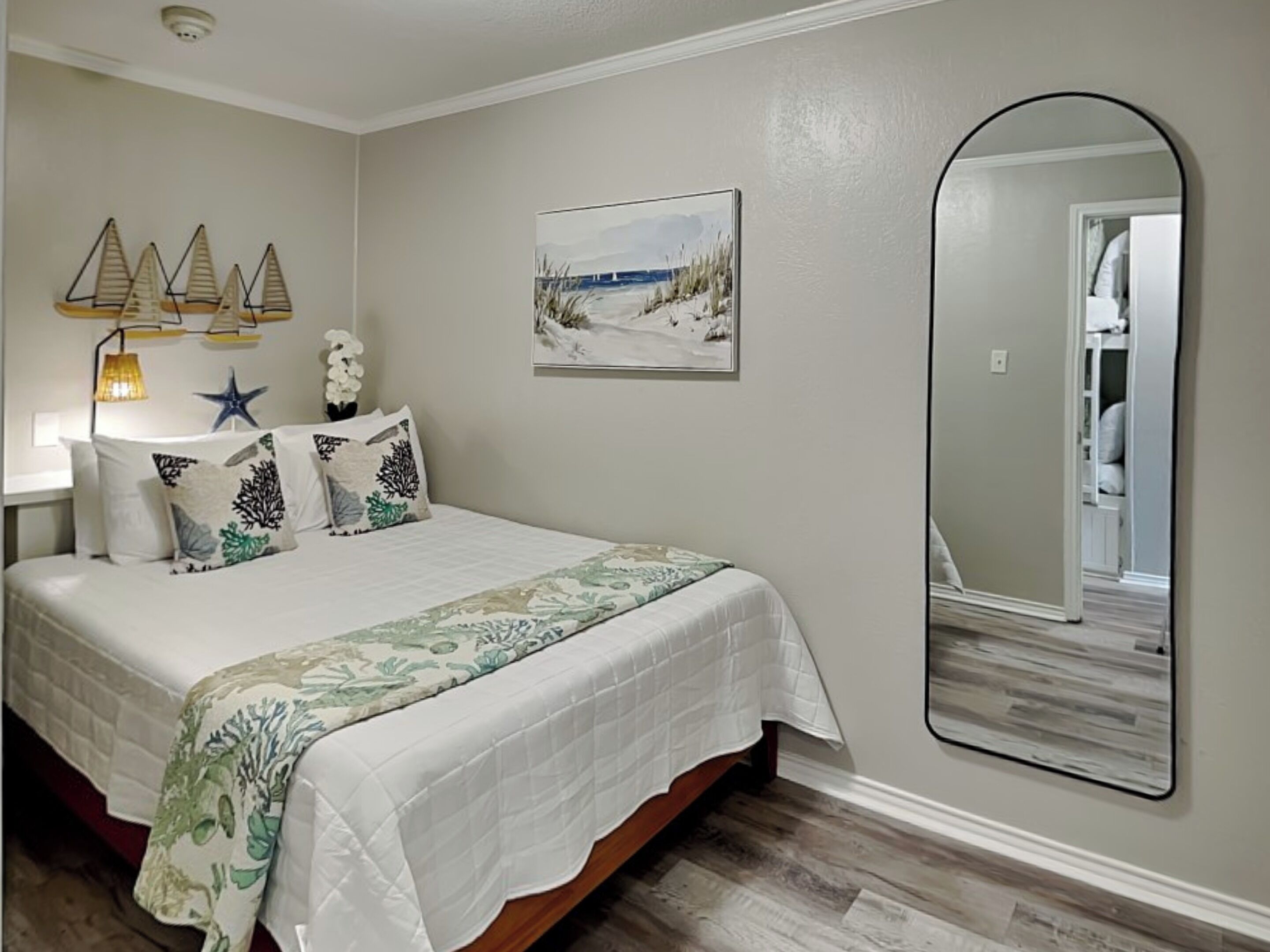 A bedroom with a bed, a large mirror, a painting, and a starfish decoration.