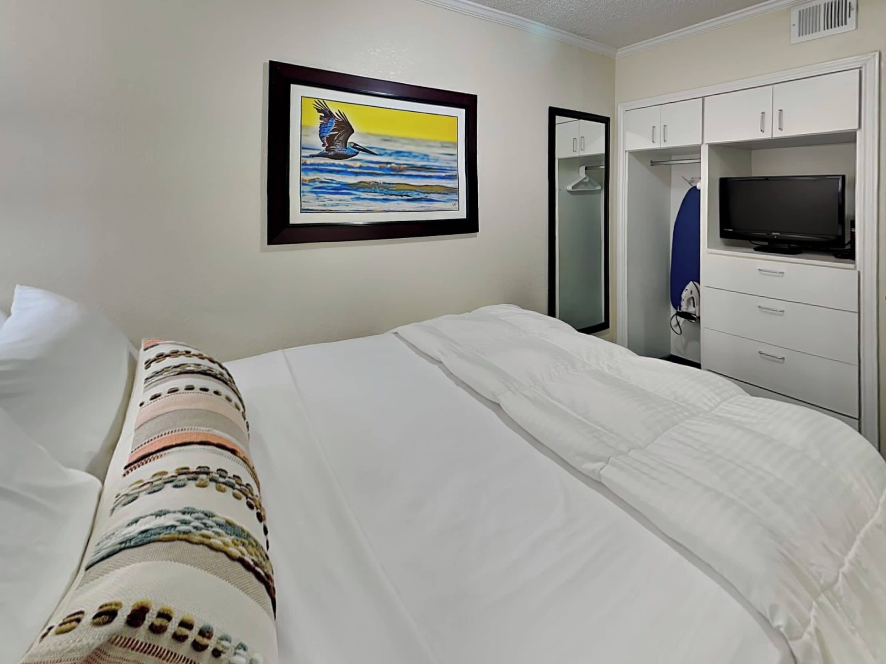 Hotelkamer met een bed, een televisie, een kledingkast en een lijst met een schilderij van een vogel boven water.