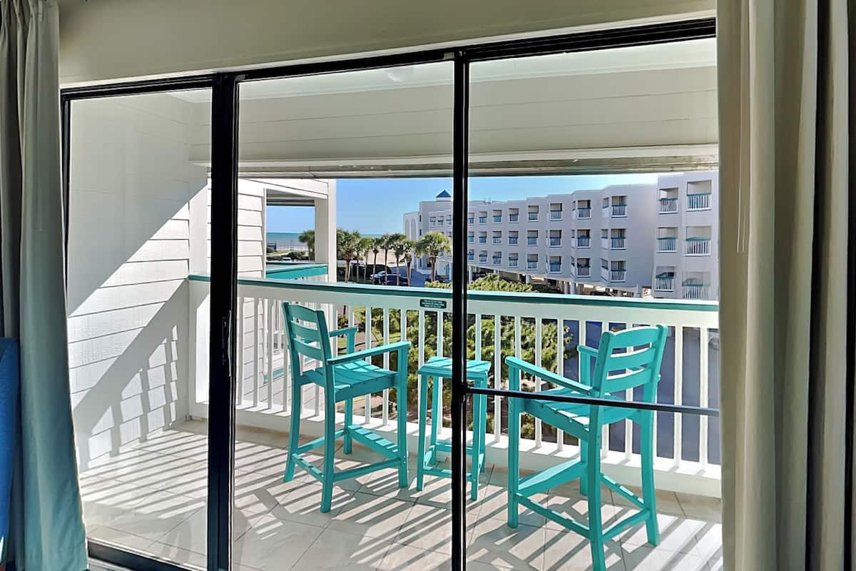 A balcony with turquoise chairs and a glass door leading to a terrace.