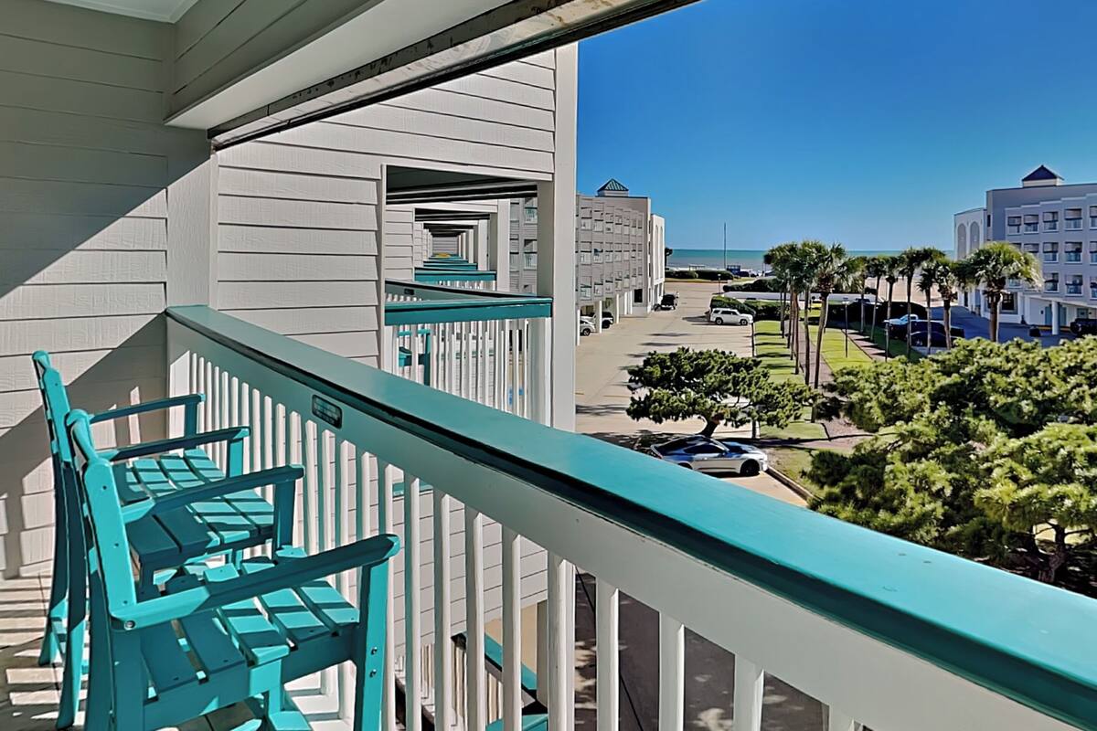 A balcony with turquoise railings overlooking a street with parked cars and buildings.