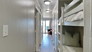A narrow hallway with bunk beds on one side and a door leading to a room. - Casa Del Mar 211 (Galveston)
