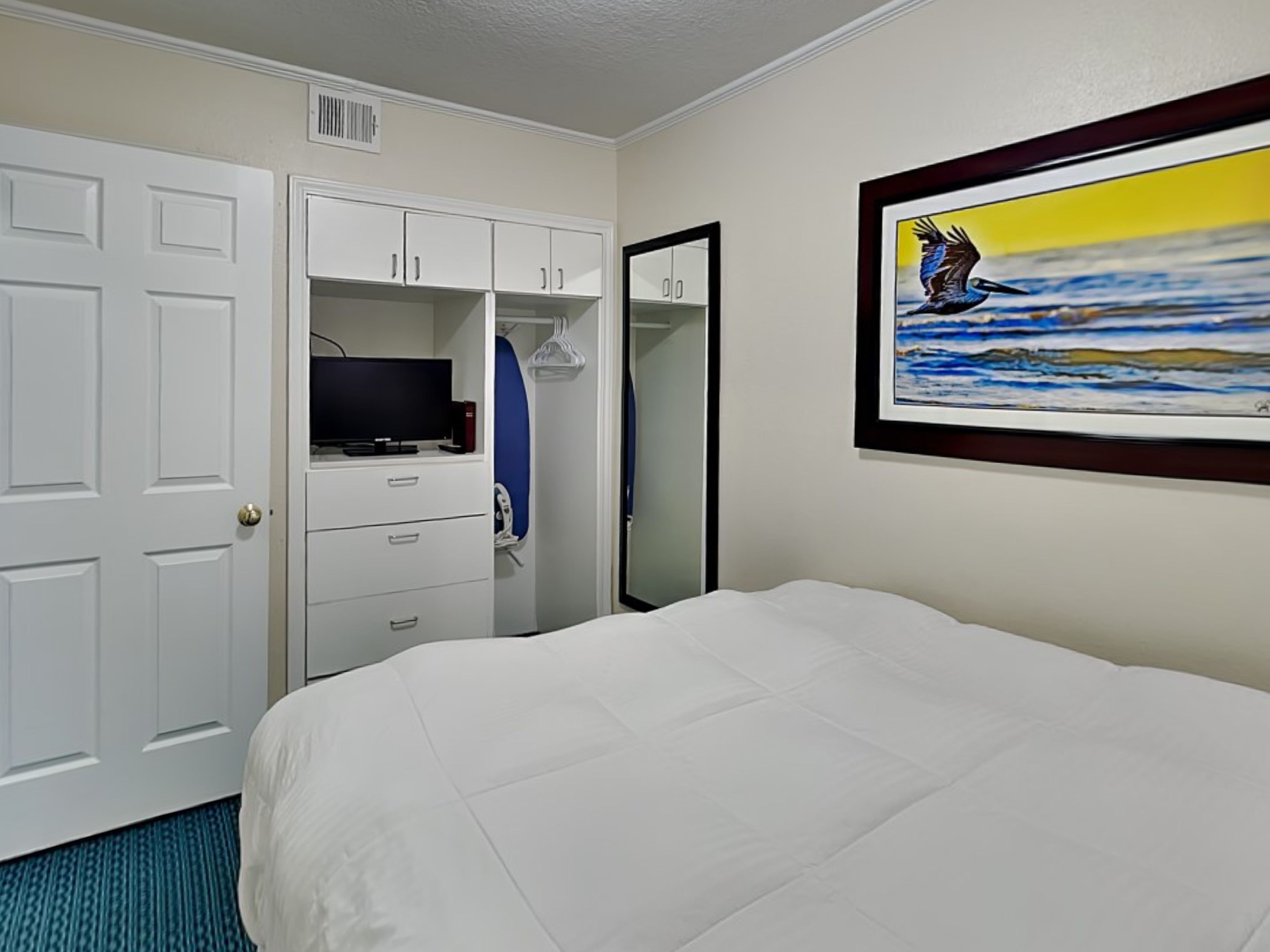 Una habitación de hotel con una cama, un televisor sobre un tocador, un espejo y un cuadro de un pájaro en la pared.