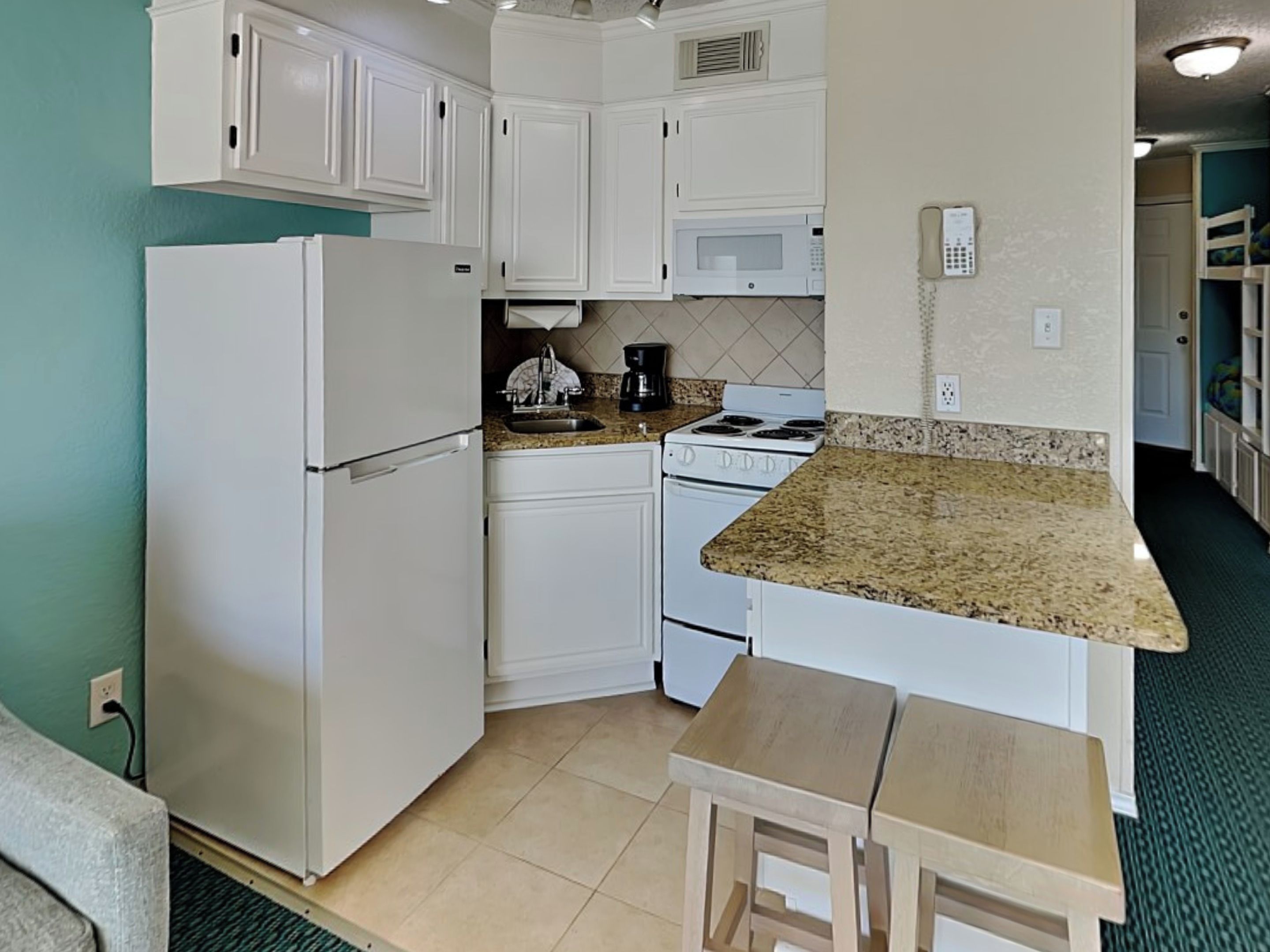 A compact kitchen with white cabinets, a refrigerator, a microwave, a stove, and a small wooden table.