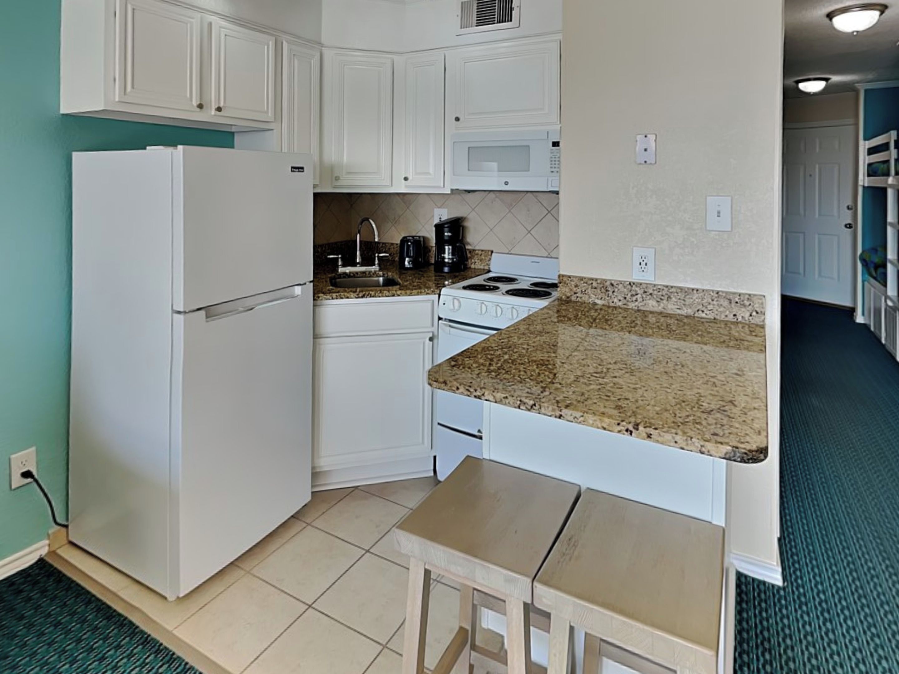 A compact kitchen with white cabinets, a white refrigerator, a microwave, a stove, and a small wooden table.