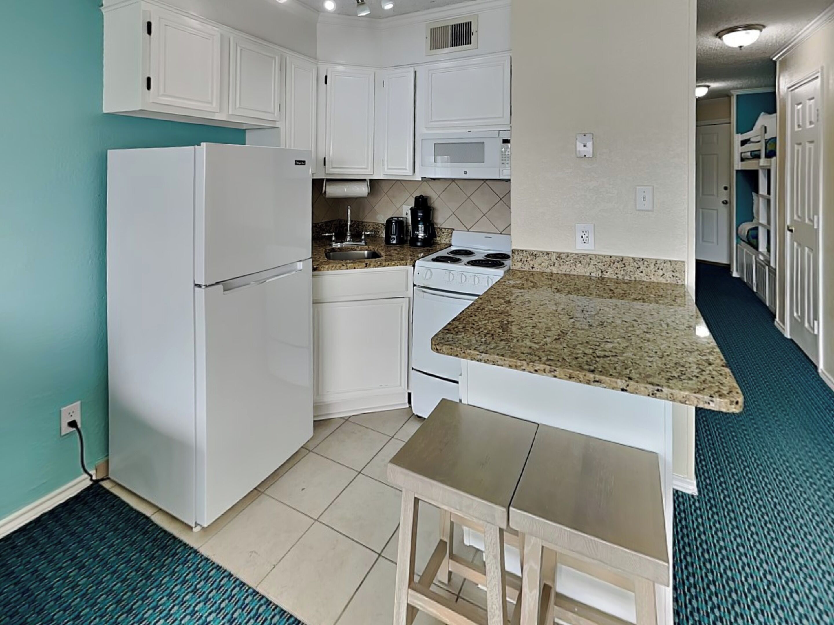 Una cocina compacta con muebles blancos, un microondas integrado, una estufa y un lavamanos.