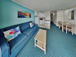 A compact living space with a sofa, a small table, a kitchenette, and a dining area.
