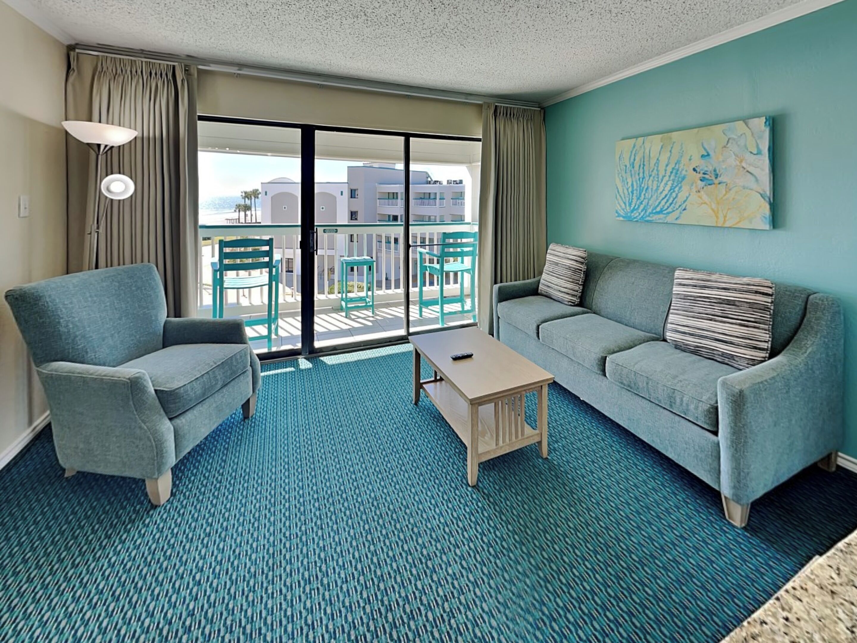 Una habitación de hotel moderna con balcón, dos sofás, una mesa de centro y un cuadro en la pared.