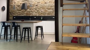 Cozinha moderna com painel de pedra, escada de madeira e área de jantar com banquetas.