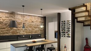 Uma cozinha moderna com revestimento de parede de pedra, iluminação pendente, espaço para vinhos e uma guitarra vermelha.