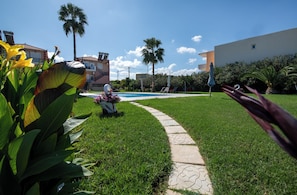 A well-maintained lawn with a curved pathway leading to a pool, surrounded by palm trees and a building with a tiled roof. - Socrates Holidays Apt. 4 with Pool near the Beach (PEO Kissamou Chanion 27, Kamisiana 730 06, Greece)