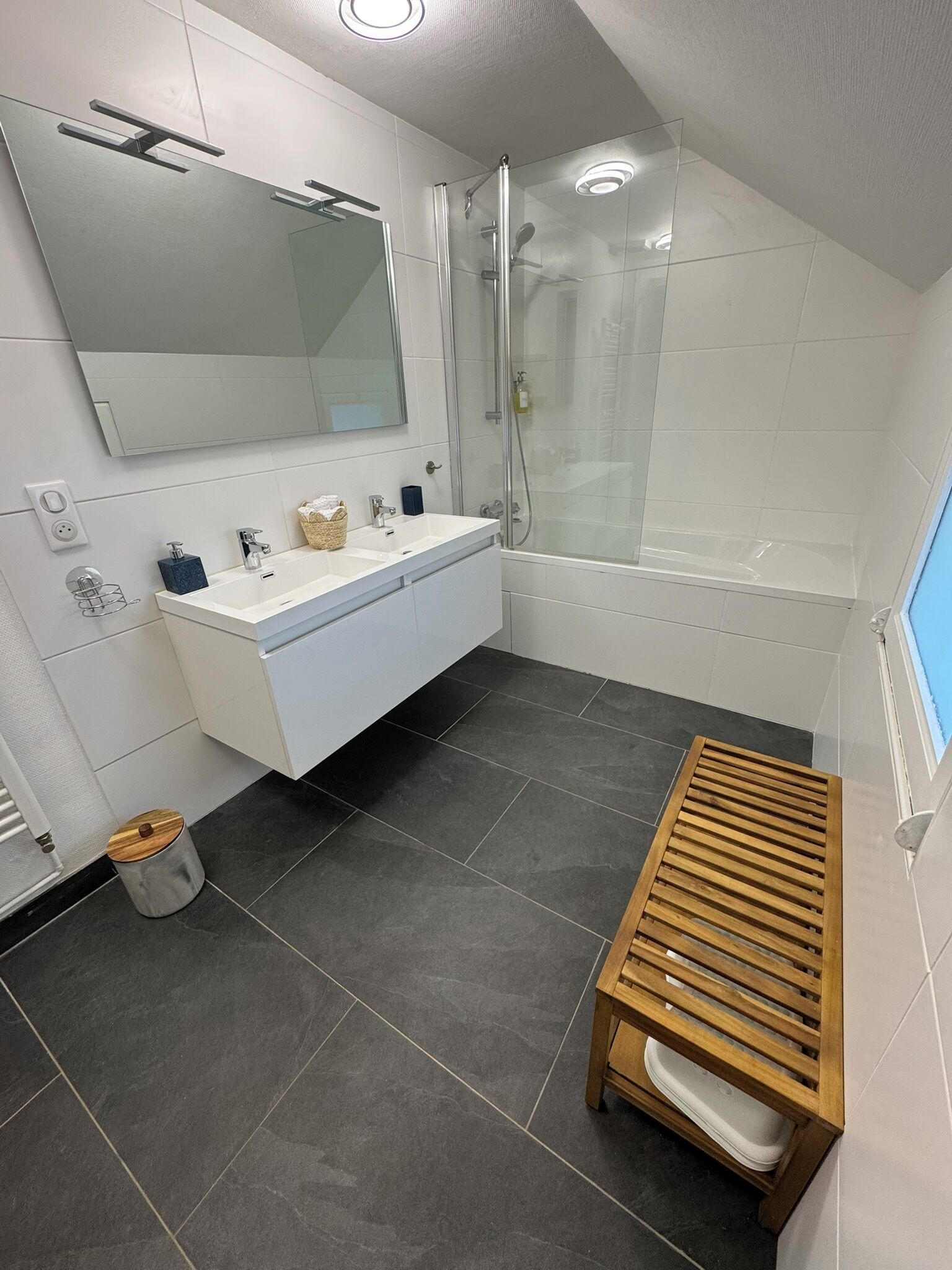 A modern bathroom with a white vanity, a glass shower enclosure, and a wooden bench.