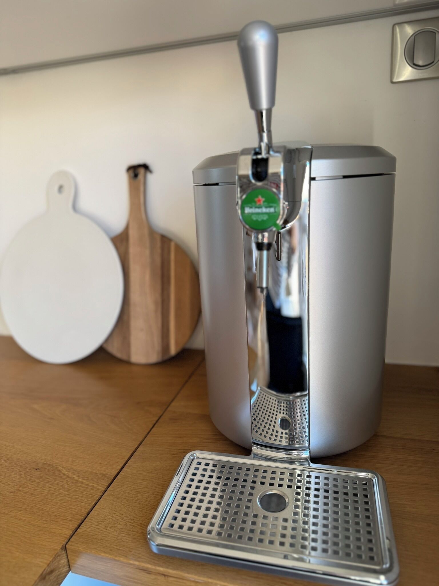 Un robinet à bière en acier inoxydable avec une étiquette verte, une râpe et une planche à découper en bois, le tout posé sur une table en bois.