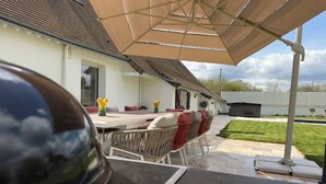 Eine Terrasse im Freien mit Tisch, Stühlen, einem Grill und einem großen Sonnenschirm.