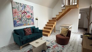 A spacious loft with a wooden staircase, a green sofa, a brown armchair, and a floral rug.