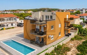 A modern multi-story building with a swimming pool, balconies, and a view of the surrounding neighborhood. - Cozy apartment in Vir with heated swimming pool (Vir)