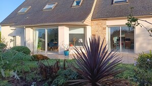 Ein modernes Haus mit schrägem Dach, großen Fenstern und einem Garten mit verschiedenen Pflanzen.