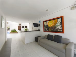 Un salon moderne avec un canapé gris, un coin cuisine doté de meubles blancs et un grand tableau représentant une fleur accroché au mur.