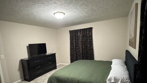 Un dormitorio con una cama, un aparador, un televisor y una ventana con cortinas.
