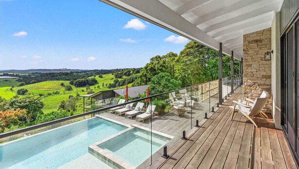 Ein moderner Poolbereich im Freien mit Glasbrüstung, Holzterrasse und Liegestühlen.