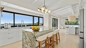 Eine moderne Küche mit einer großen Kochinsel, Barhocker und Blick ins Freie.