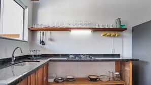 A kitchen with a granite countertop, a stainless steel sink, a gas stove, and a wooden shelf above holding various kitchenware. - House w/ 3 Bedrooms and Barbecue Lpb0000 (Garopaba)