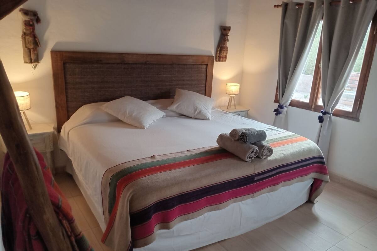 A neatly made bed with a striped blanket and rolled towels, a wooden headboard, and two bedside lamps.