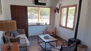 A cozy living room with a sofa, a coffee table, and two chairs. There is a wooden table with a lamp, a wicker basket, and a small table with a decorative item. - Cabañas La Nochera (Tilcara)
