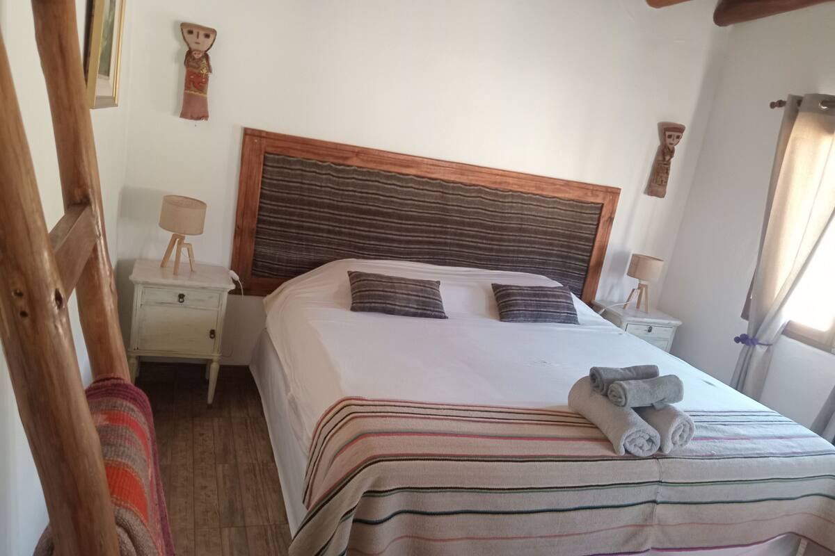 A neatly made bed with striped bedding and rolled towels, a wooden headboard, and bedside tables with lamps.