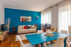 A modern living room with a blue accent wall, a sofa, a dining table, and a coffee table. - Sesto Sole - wide 6th Floor Apart near Prada-Bocconi-IEO (Milano)