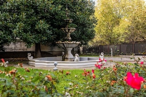 Ein Garten mit einem Brunnen, umgeben von Bäumen und einem Zaun.