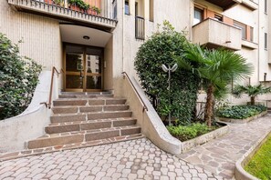 A building entrance with a set of stone steps leading to a glass door, surrounded by greenery and a paved pathway. - Sesto Sole - wide 6th Floor Apart near Prada-Bocconi-IEO (Milano)