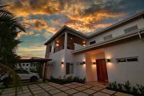 A modern house with a white exterior, a covered porch, and a car parked in the driveway. - Modern Comfort Just Minutes from West Bay Beach (West Bay)