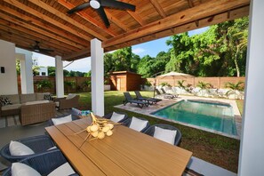 An outdoor patio with a wooden table, wicker chairs, and a pool. - Modern Comfort Just Minutes from West Bay Beach (West Bay)