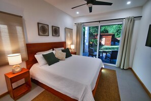 A bedroom with a large bed, a nightstand with a lamp, a ceiling fan, and a view of a patio with outdoor furniture. - Modern Comfort Just Minutes from West Bay Beach (West Bay)