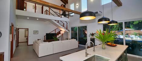 Ein geräumiger Wohnbereich mit einem weißen Sofa, einer Kücheninsel mit Spüle und einer Treppe, die in eine obere Ebene führt.