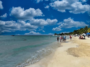 A beach with clear turquoise water, people walking along the shore, and a boat in the distance. - Modern Comfort Just Minutes from West Bay Beach (West Bay)
