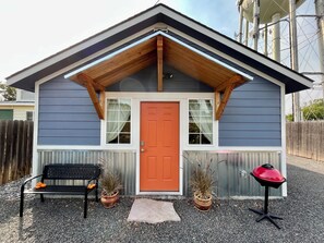 Ein kleines Haus mit roter Tür, einer Holzveranda und einem Grill im Vorgarten.