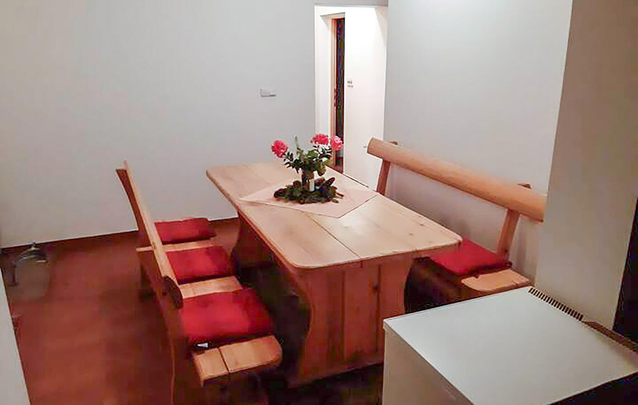 A small dining area with a wooden table and six chairs, each with a red cushion. There is a small white table on the right side of the image.