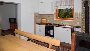 A compact kitchen with a stove, sink, and cabinets. There's a window with a curtain, a bench, and a fireplace. - 2 bedroom nice apartment in Mrkopalj (Mrkopalj)