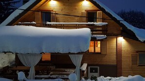 Una cabaña de madera con balcón, cubierta de nieve e iluminada desde el interior.