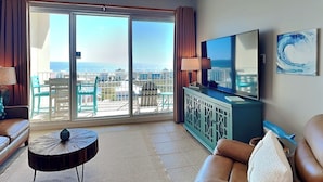 Ein geräumiges Wohnzimmer mit Balkon, einem Flachbildfernseher und Blick auf den Ozean.