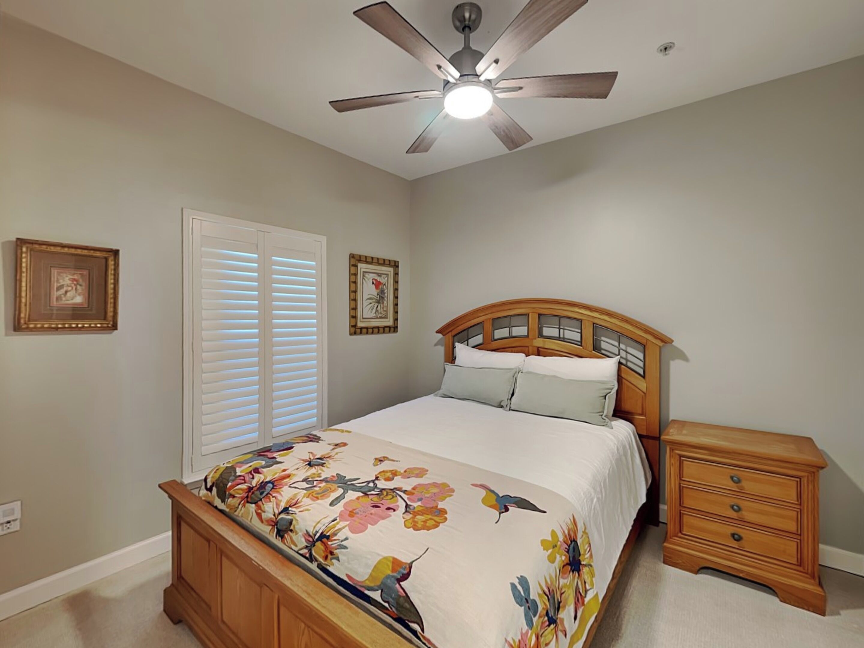 A bedroom with a bed, a nightstand, a ceiling fan, and two wall-mounted picture frames.