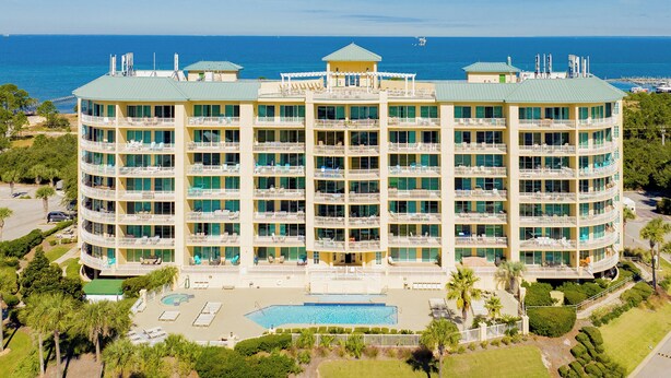 Ein mehrstöckiges Hotel mit Pool, umgeben von viel Grün und mit Blick auf den Ozean.