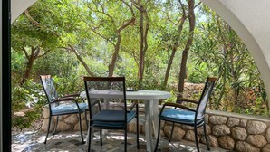 An outdoor patio with a round table and four chairs, surrounded by a stone wall and lush greenery. - Apartment in Novalja (127) (Novalja)