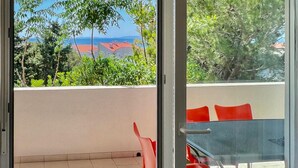 Un balcon avec une table et des chaises, une vue sur la mer et de la verdure.