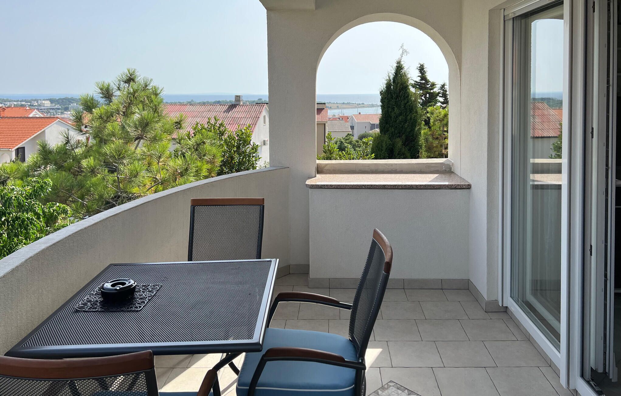 Un balcon avec une table et des chaises, une vue sur la ville et une porte vitrée.