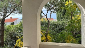 Janela em arco com vista para uma paisagem costeira, incluindo árvores e um edifício com telhado vermelho.